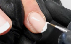 A Nail Tech painitng a French Tip onto a pink nail using a fine Striper Brush